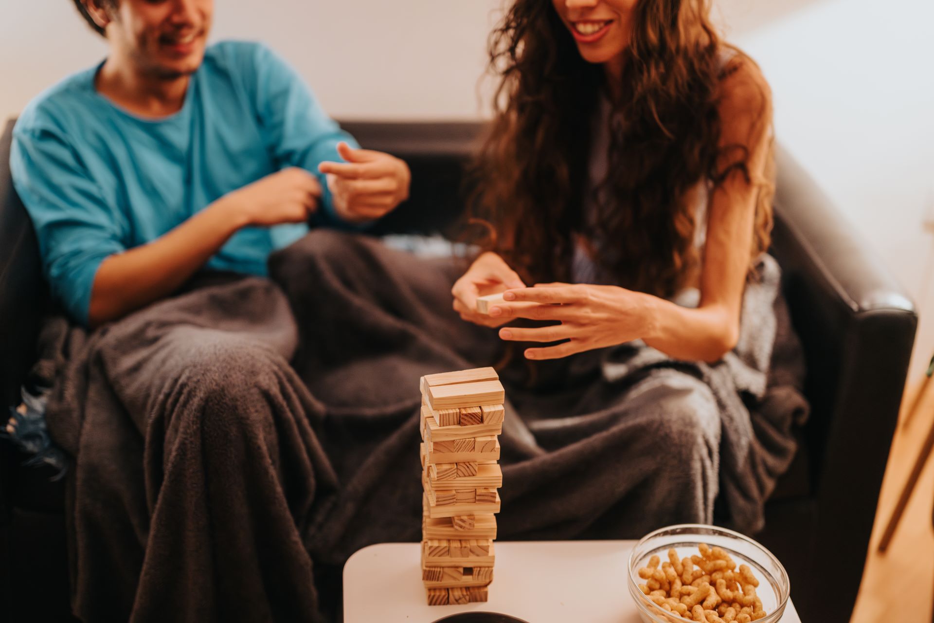 Paar spielt Jenga auf dem Sofa, eingekuschelt in eine weiche Alpaka-Decke.